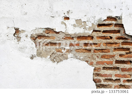 Background of an old wall with damage to the white plaster revealing red bricks. Background of an old wall with damage to the white plaster revealing red bricks. 133753061