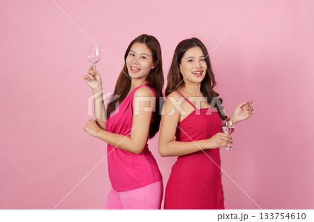 Party Celebration. Two joyful women toasting with glasses in vibrant pink attire. 133754610