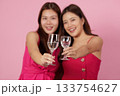 Party Vibes. Two women clinking glasses in celebration against a pink backdrop. 133754627