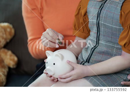 Financial Education. Parent and child engaging in saving money with piggy bank. Financial Education. Parent and child engaging in saving money with piggy bank. 133755592