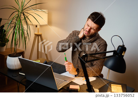 Man with neck pain working at desk in home office Man with neck pain working at desk in home office 133756052