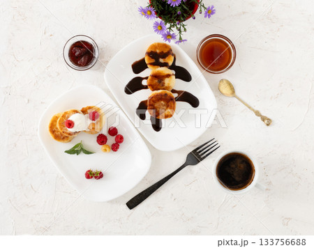 Cup of coffee and curd fritters with sour cream, berries and chocolate on the porcelain plates. Cup of coffee and curd fritters with sour cream, berries and chocolate on the porcelain plates. 133756688