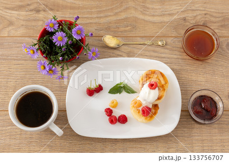 Cup of coffee and curd fritters with sour cream and berries on the porcelain plates. Cup of coffee and curd fritters with sour cream and berries on the porcelain plates. 133756707