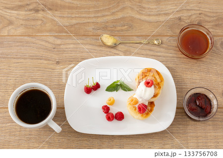 Cup of coffee and curd fritters with sour cream and berries on the porcelain plates. Cup of coffee and curd fritters with sour cream and berries on the porcelain plates. 133756708