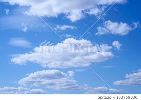 White clouds in a blue sky. A natural background of a light summer sky for graphic design. Horizontal photo. White clouds in a blue sky. A natural background of a light summer sky for graphic design. Horizontal photo. 133758030