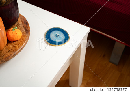 Blue agate coaster placed on the side of a white coffee table in a simple everyday home setting, mixing natural stone with clean modern decor. Concept of energy, grounding, spirituality, minimalism. 133758577