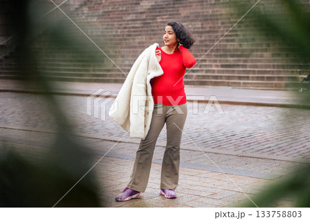 indian woman in red sweater holding winter coat on city street in helsinki indian woman in red sweater holding winter coat on city street in helsinki 133758803