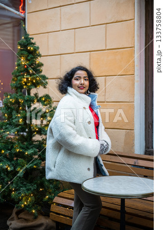 indian woman in winter coat standing by decorated christmas tree in helsinki indian woman in winter coat standing by decorated christmas tree in helsinki 133758804