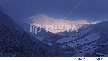Aerial photo of snowy alpine peaks in Austria with a glacier rising through morning mist. Blue sky, sunlight, and conifer forests in the foreground create a peaceful winter atmosphere. Aerial photo of snowy alpine peaks in Austria with a glacier rising through morning mist. Blue sky, sunlight, and conifer forests in the foreground create a peaceful winter atmosphere. 133758948