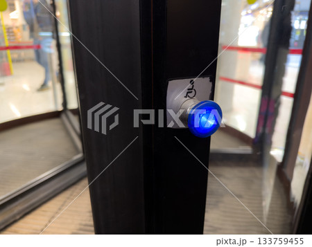 Button for people with disabilities at entrance to revolving door. Press button to slow down revolving glass doors for access to building. Special button to assist people with limited mobility Button for people with disabilities at entrance to revolving door. Press button to slow down revolving glass doors for access to building. Special button to assist people with limited mobility 133759455