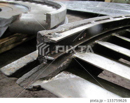 Close-up view of damaged metal component, possibly from turbine or industrial machinery. Jagged edges, evidence of repair work, like welding, are visible on the worn surface. Restoration of diaphragms 133759626