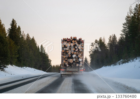 logging truck driving on snowy forest road in winter lapland 133760480