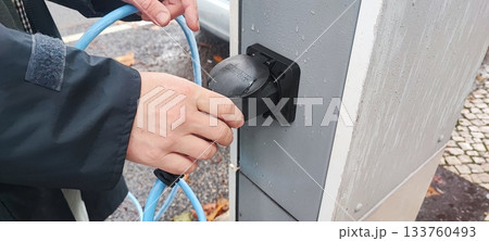 Human hand connecting an electric vehicle charging cable to a public charging station. Concept: electric vehicle infrastructure, clean energy, charging technology, eco-friendly transport. Human hand connecting an electric vehicle charging cable to a public charging station. Concept: electric vehicle infrastructure, clean energy, charging technology, eco-friendly transport. 133760493