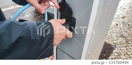 Human hand connecting an electric vehicle charging cable to a public charging station. Concept: electric vehicle infrastructure, clean energy, charging technology, eco-friendly transport. 133760494