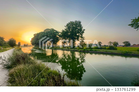 Serene countryside sunset with reflective trees and gentle mist 133761299