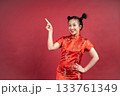 Happy Asian woman in Cheongsam pointing finger at copy space on red background. Happy Asian woman in Cheongsam pointing finger at copy space on red background. 133761349