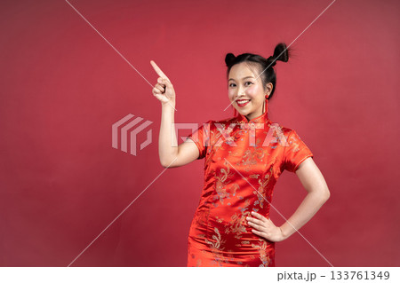 Happy Asian woman in Cheongsam pointing finger at copy space on red background. Happy Asian woman in Cheongsam pointing finger at copy space on red background. 133761349