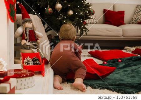 Baby in cozy pajamas crawling on floor near decorated Christmas tree, surrounded by festive pillows and holiday decorations. Warm and intimate holiday scene perfect for family and seasonal themes. Baby in cozy pajamas crawling on floor near decorated Christmas tree, surrounded by festive pillows and holiday decorations. Warm and intimate holiday scene perfect for family and seasonal themes. 133761368