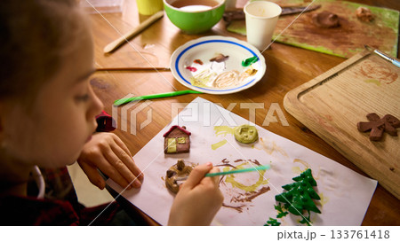 Child painting multiple clay figures arranged on paper during creative workshop 133761418