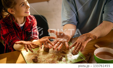 Girl showing muddy clay hands with father during sculpting practice Girl showing muddy clay hands with father during sculpting practice 133761455