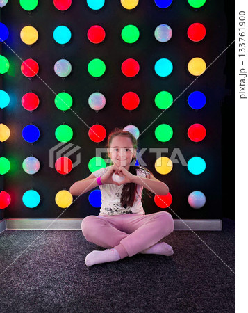 Girl making heart hands gesture against colorful lights Girl making heart hands gesture against colorful lights 133761900