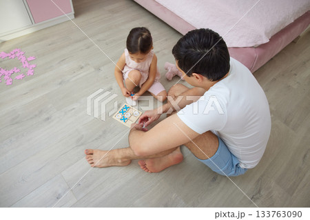 Father and daughter enjoying quality time playing a tic-tac-toe board game on the floor 133763090