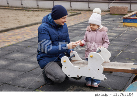 Father playing with toddler daughter on a seesaw at an outdoor playground in winter Father playing with toddler daughter on a seesaw at an outdoor playground in winter 133763104