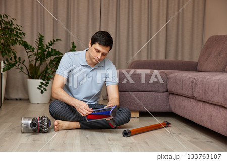 Man sitting on floor assembling parts of a vacuum cleaner 133763107