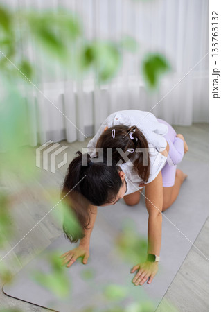 Mother doing yoga pose with her daughter on her back at home 133763132
