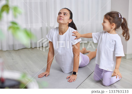 Mother and daughter doing yoga exercise on a mat, daughter touching mother's shoulder Mother and daughter doing yoga exercise on a mat, daughter touching mother's shoulder 133763133