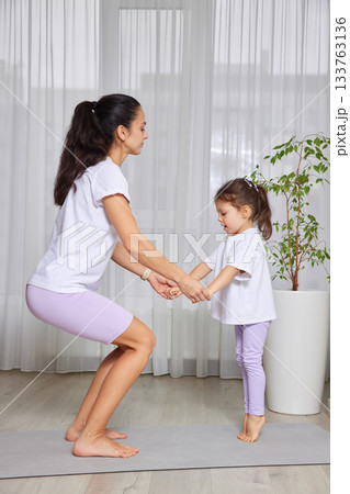 Mother and daughter exercising together on a yoga mat, doing a squat 133763136