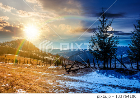 countryside mountain landscape on spring equinox. day and night time change concept. spruce trees and fence on meadow with snow under sun and moon. snowy distant ridge. duality and transition template countryside mountain landscape on spring equinox. day and night time change concept. spruce trees and fence on meadow with snow under sun and moon. snowy distant ridge. duality and transition template 133764180