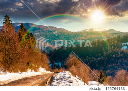 country road winding through winter landscape under blue sky at sunset. mountains in evening light. travel background with snow covered slopes. storytelling cinematic image under the rainbow country road winding through winter landscape under blue sky at sunset. mountains in evening light. travel background with snow covered slopes. storytelling cinematic image under the rainbow 133764188