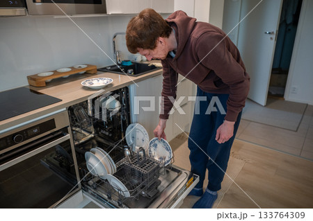 man unloading clean dishes from dishwasher in modern bright kitchen man unloading clean dishes from dishwasher in modern bright kitchen 133764309