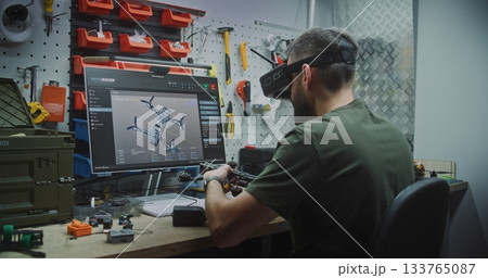 Engineer Wearing FPV Goggles Simultaneously Designing Drone on Screen and Assembling Workbench 133765087