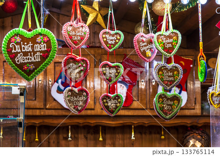 Colorful gingerbread heart display at christmas market. Festive assortment of lebkuchenherzen hangs in rows with german phrases Ich liebe dich, Fuer dich, and Bester opa. 133765114
