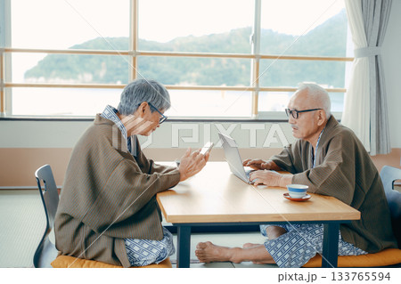 旅館の和室でパソコンとスマホを使うシニア夫婦 133765594