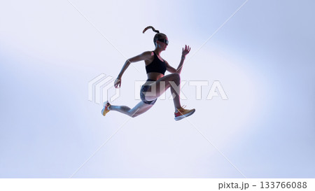 Futuristic athlete in dynamic mid-air leap against gradient light 133766088