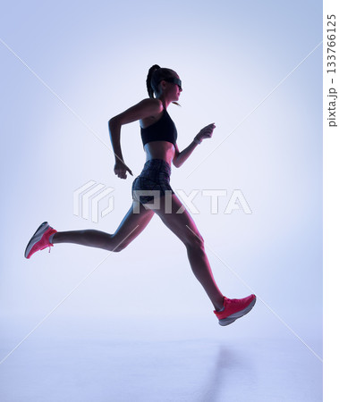 Female runner in neon studio jumping with strong athletic extension 133766125