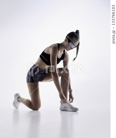 Athletic woman kneeling to tie running shoes before workout in studio Athletic woman kneeling to tie running shoes before workout in studio 133766183
