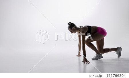 Female sprinter in starting position on minimal white background Female sprinter in starting position on minimal white background 133766204