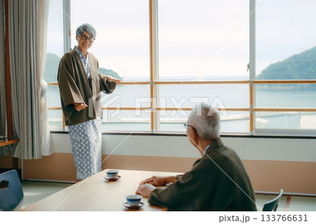 窓辺で手を振る高齢女性と見守る夫の旅館シーン 窓辺で手を振る高齢女性と見守る夫の旅館シーン 133766631