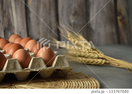 Eggs in a paper tray Placed on wicker and concrete floors. Garnish with dried barley. There is a background of blurry wooden planks. 133767080