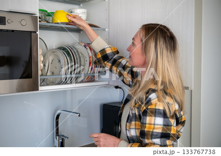 woman organizing clean dishes in kitchen cabinet woman organizing clean dishes in kitchen cabinet 133767738