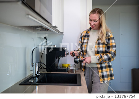 woman preparing coffee with home espresso machine in bright modern kitchen woman preparing coffee with home espresso machine in bright modern kitchen 133767754