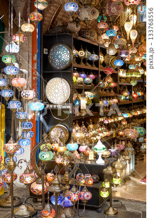 A vibrant shop displays an array of colorful, intricate mosaic lamps, radiating warmth and beauty in a bustling market. 133768556