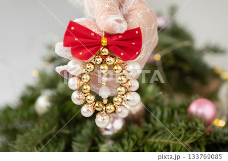 Elegant christmas ornament held by gloved hand against decorated tree background Elegant christmas ornament held by gloved hand against decorated tree background 133769085