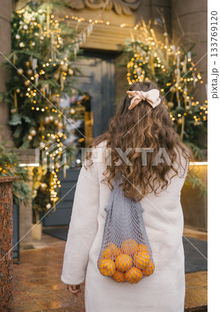 Young caucasian female carrying oranges in mesh bag during festive holiday season 133769120