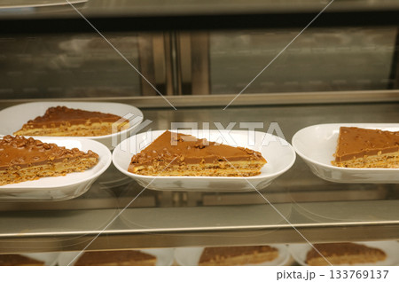 Slices of rich caramel cake on display in a bakery case 133769137