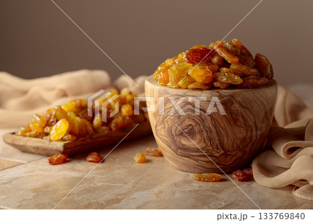 Yellow sultana raisins in a wooden bowl on a beige background. 133769840